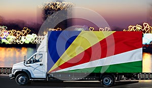 Seychelles flag on the side of a white van against the backdrop of a blurred city and river. Logistics concept