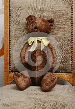 shabby teddy bear with a yellow bow on his neck sitting in an old armchair