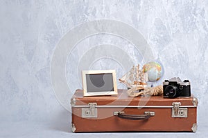 Shabby vintage suitcase with summer marine accessories on grey background. Picture frame, globe, camera, toy sailboat, sea rope. T