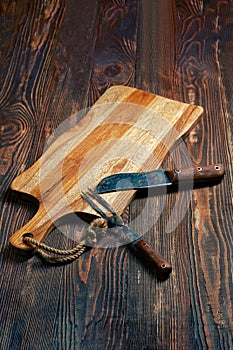 Shabby wooden table with empty cutting board and old knife and fork for barbecue