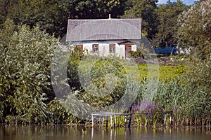 Shabby and worn old country house ruining lonely, abandoned home and yard on bank of countryside lake