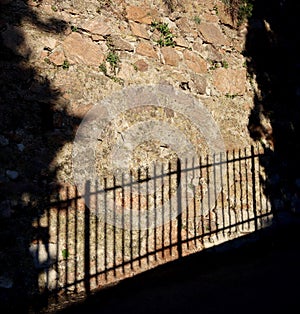 A shadow of a fence cast against an old brown brick wall photo