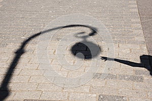 The shadow of the girl reaches for the lamppost on the asphalt