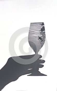 Shadow of a hand holding a glass on a white background. Sun glare from the glass.