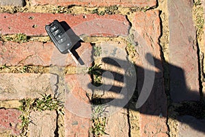 shadow of a hand on a red sidewalk trying to catch a car black key. A robber projects the silhouette of his hand and fingers on