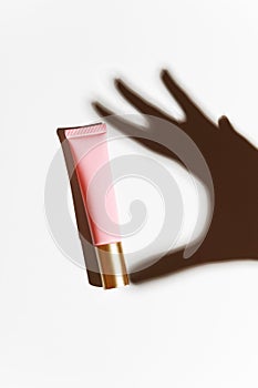 Shadow hands with a pink tube of moisturizing scream on a white background. The attribute of facial and hand care. Tonal,
