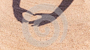 Shadow from hands in the shape of heart on the sand on beach with space for the text. Sea travel and holiday.