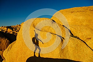 Shadow of a hiker woman climbing the rocks in a beautiful warm sunset light in the Joshua Tree National Park, California, USA