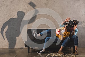 Shadow of man holding axe and scared couple with popcorns using virtual