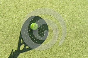 Shadow of a padel racket with a yellow ball on the green grass.