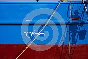 shadow of painter climbing ladder with white plimsoll mark on blue and red rust proof steel hull surface of fishing vessel