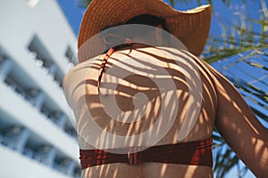 Shadow of palm leaves on back of beautiful woman in hat relaxing at pool. Skin care and sunscreen