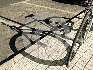 Shadow of parked bicycle over the asphalt road