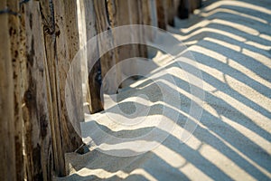 Shadow patterns in the beach sand along a wooden fence