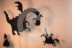 Shadow Puppets of Dragon, Princess and Knight with bright glowing screen of shadow theatre in the background.