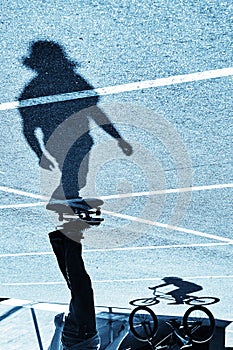 Shadow of a skateboarder and bicycler on asphalt. Blue toning