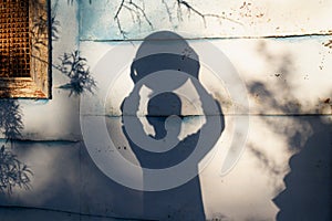 The shadow of a teenage boy holds a large round ball over his head