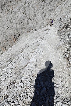Shadow on the trail of the hiker with hat and a young woman walking in the mountains
