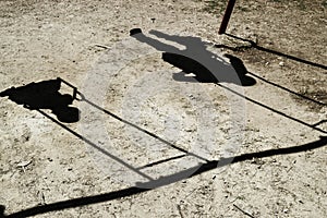 Only the shadow of two children is visible children ride on a swing