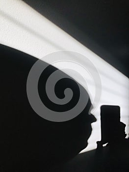 Shadow on the wall.  A man's head looks at the phone.