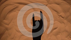 Shadow of a woman's hand on sand of beach showing rock gesture. Close up silhouette of a female hand. Summer holiday