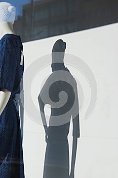 Shadow of a woman`s mannequin in a blue dress in a shop window