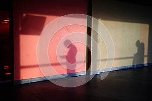 The shadow of a young passerby on a stone wall. Sunlight creates a drawing of a person. The man looks at the smartphone