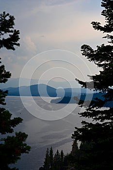 Shadowed Evergreen Trees near windy lake and blue mountains