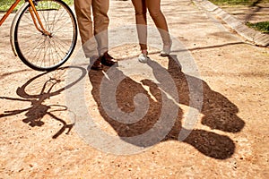 Shadows of couple standing in the park alley with bicycle and a