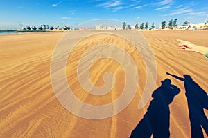 Shadows on the golden sand - two people take picture of Essaouira port