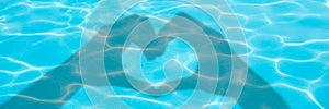 Shadows of hands forming a heart on blue swimming pool water background panoramic valentines day or summer banner