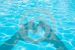 Shadows of hands forming a heart on blue swimming pool water, summer concept