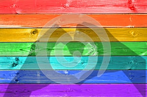 Shadows of hands forming a heart on colorful rainbow painted wood planks background, gay flag love concept