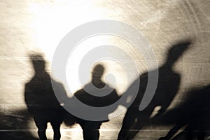 Shadows silhouettes of three men walking on sunset promenade