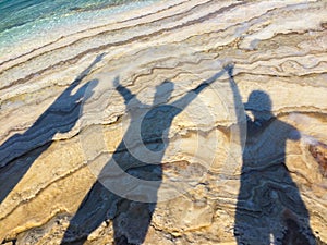 Shadows of three happy people at beach raising hands