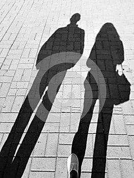 Shadows of two people, a man and a woman, walking along a tiled pavement