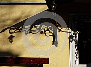 Shadows from a visor over the entrance and a street lamp in a retro style on a stucco wall of a building