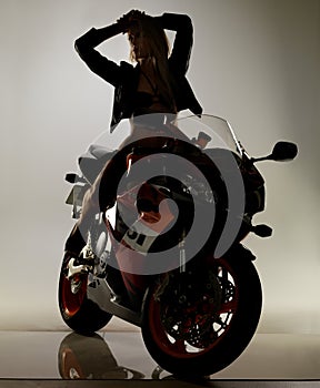 Shadowy seductress on her iron beast. Stunning young woman in a bikini and leather jacket sitting on a motorcycle with