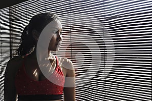 Shady portrait of young beautiful Asian woman in gym sport cloths looking through Venetian blinds