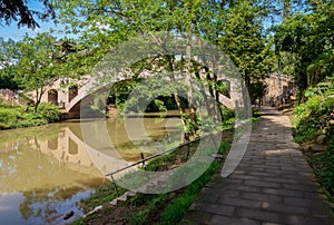 Shady riverside path before arch bridge in sunny autumn