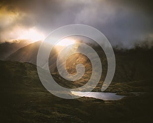 Shafts of sunlight breaking through the clouds near mountain tarn in the Lake District, England