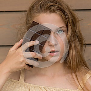 A shaggy, beautiful Girl with red hair and freckles holds a chocolate bar in her hand and looks at the camera against a wooden