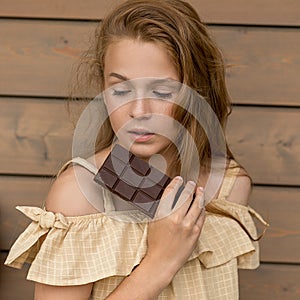 A shaggy beautiful Girl with red hair and freckles holds a chocolate bar in her hands and looks down on a wooden background of