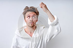 shaggy confused guy in bathrobe isolated on white background, touches long regrown hair