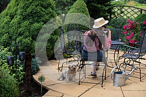 A shaggy dog sits on the terrace and a girl sits on a chair and drinks coffee from a cup.