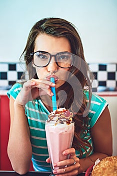 Shake it up. Cropped portrait of an attractive young woman enjoying a milkshake in a retro diner.