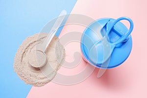 Shaker and scoop with chocolate protein on pink and blue background, top view.