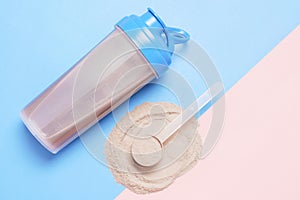 Shaker and scoop with chocolate protein on pink and blue background, top view.