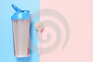 Shaker and scoop with chocolate protein on pink and blue background, top view.