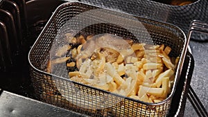 Shaking french fries in a wire basket then immerse them in boiling hot oil again